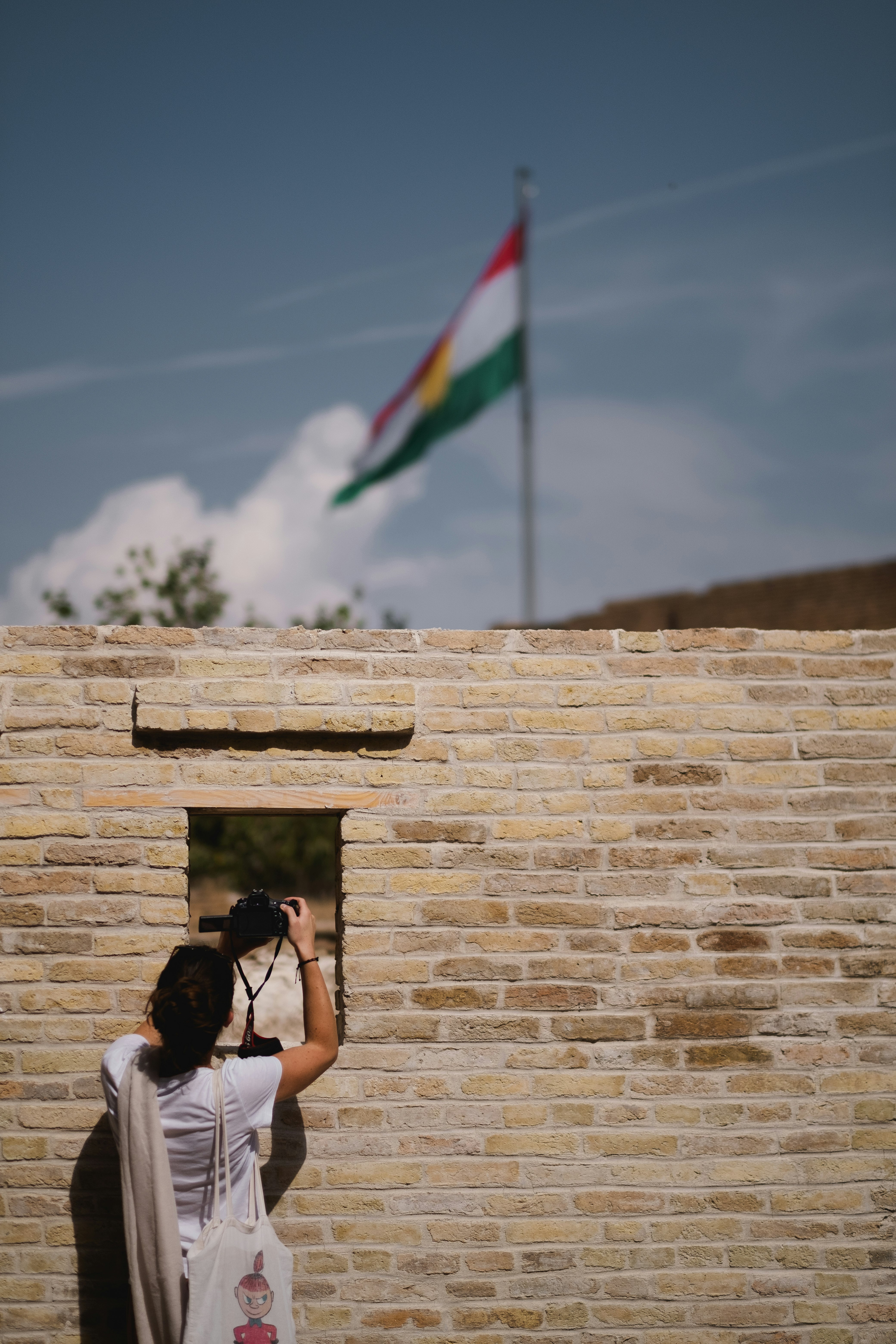 woman in white t-shirt leaning on brown brick wall during daytime